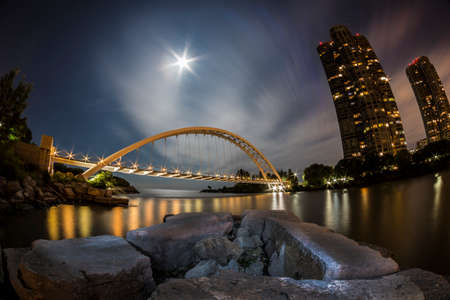 Illuminated arch bridge at night with a harvest moon.の写真素材