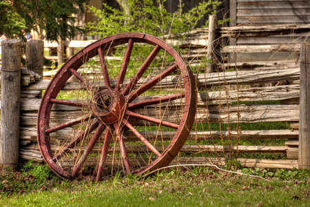 A single rustic wagon wheel leaning against wooden fence.の写真素材
