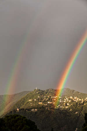 Double rainbow over the mountain overlooking Como. City of Brunate in summertime. Como Lake. Italyの写真素材
