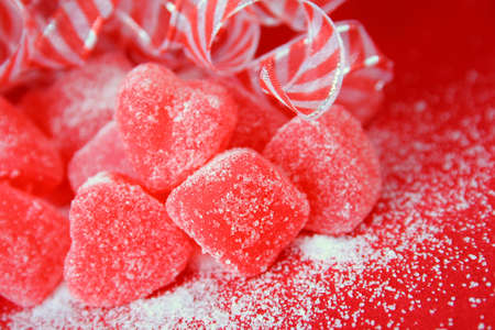 red heart candy covered in sugar with red and white ribbons in the background all on a red background.の写真素材