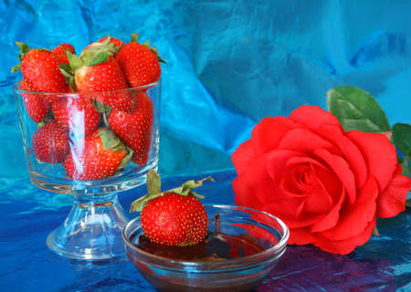 \r\nGrouping of strawberries, chocolate sauce and a rose all on a metallic blue background.の写真素材