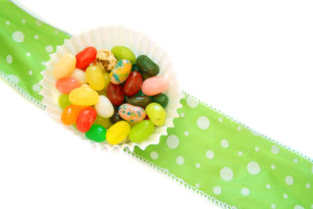Jelly beans in a muffin cup sitting on a lime green ribbon on a white background.