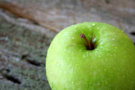 Close up of a wet green apple on a wood textured background.の写真素材