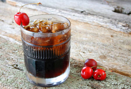 A glass of cherry soda and ice cubes with fresh ripe cherries as a garnish.の写真素材