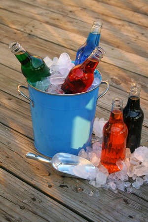An assortment of flavored sodas in an ice bucket with some on the side and ice that has spilled out onto the deck.の写真素材
