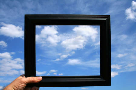A person holding up a picture frame against a beautiful blue sky full of clouds.の写真素材