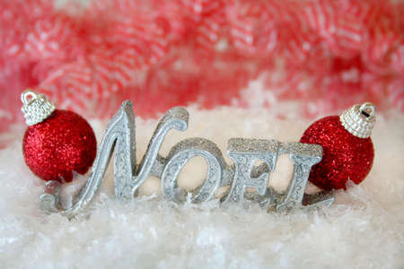The word Noel made of glitter sitting in the middle of fake snow with two red christmas ornaments on each end.  Used selective focus and a shallow depth of field.の写真素材