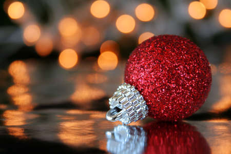 A red Christmas ornament on a reflective background with blurred lights to the far back. Copy space...