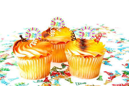 Three cupcakes with confetti all on a white background.  The cupcakes have a decoration with the word party on them. Used a shallow depth of field and selective focus.の写真素材