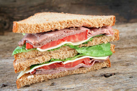 Fresh roast beef sandwich with Swiss cheese, tomato, lettuce on rye bread with a wood textured background for a rustic look.の写真素材