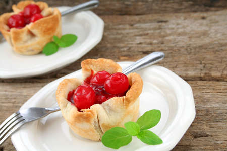 Mini individual cherry tarts/pies on white plates and garnished with mint leaves.  Used a wood textured background for a rustic look.の写真素材