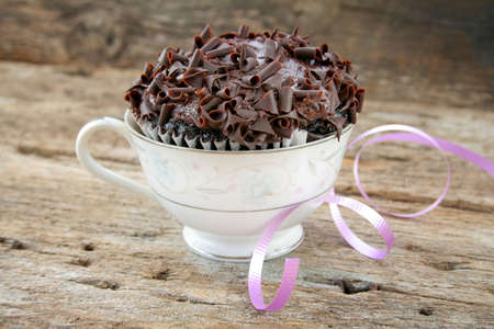 Chocolate cupcake in a china cup with a colorful curled ribbon laying to the side.の写真素材