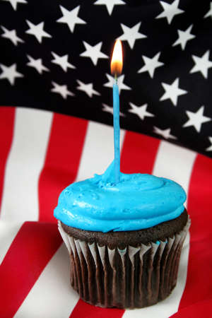 Chocolate cupcake with blue icing and a blue candle burning.  An American flag is the background.の写真素材