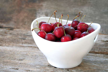 Fresh cherries in a white bowl sitting on an old wood table and room for text.