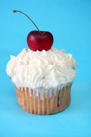 One cupcake with white icing and a cherry on top shot on a blue background.の写真素材