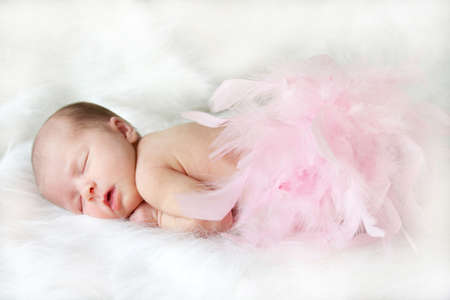 sleeping infant on white with pink feathers covering her bottom.の写真素材