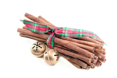 Cinnamon sticks tied with Christmas ribbon and with two jingle bells to the side on a white background with room for your text.の写真素材