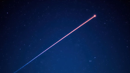 A brilliant meteor streak with a glowing tail in a star-filled night sky.の素材