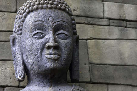 close up of a buddha statue head against a stone wallの写真素材