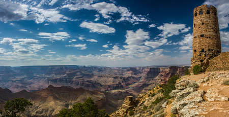 Panorama of the grand canyon with a blue sky and white clouds and the Desert View watchtower to the right of the imageの写真素材