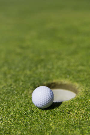 close up of a white golf ball on the edge of a hole with out a flagの写真素材