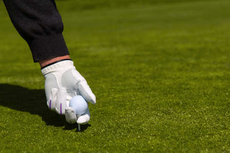 A close up of a golfer with a white glove placing a ball on a tee の写真素材