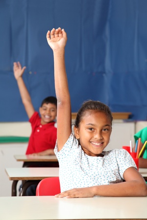 Two smiling young school children arms raised in classの写真素材