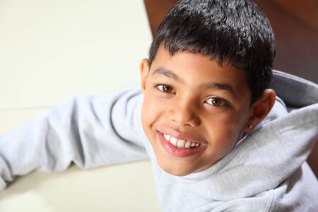 Smiling young ethnic school boy wearing grey sweater in classroom