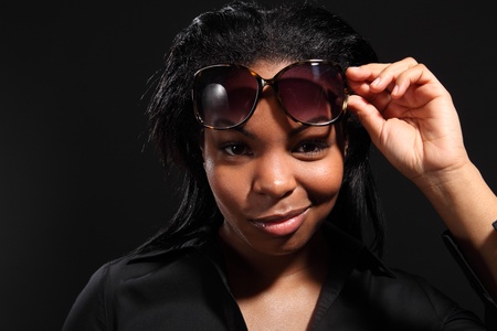 Fun smiling headshot from beautiful young black woman, holding dark sunglasses on her head and wearing black shirt.の写真素材