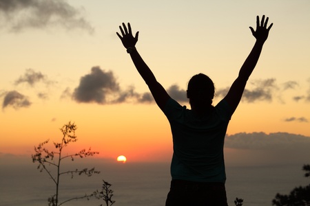 Woman hiker in silhouette standing arms raised to sunsetの写真素材