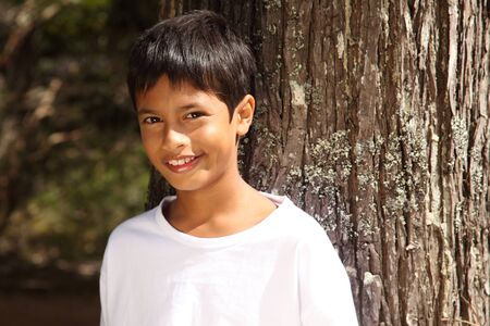 Close up young boy big smile leaning against a treeの写真素材