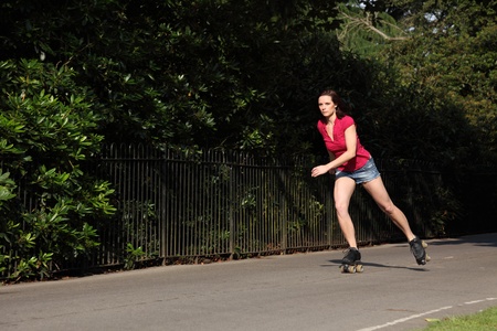 Leisure activity for fit beautiful young athletic woman roller skating through the park in summer sunshine. She is wearing a red top and denim cut off shorts showing off her long legs.の写真素材