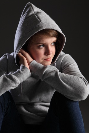 Depressed young teenager girl sitting alone on floor looking sad, stressed and frightened. She is wearing jeans and a grey hoodie and a worried expression.の写真素材