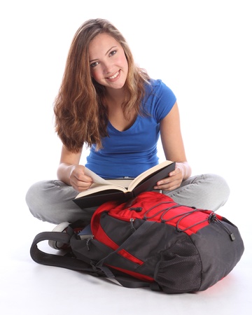 Study time for beautiful high school teenage student girl reading education book sitting cross legged on floor, with school rucksack wearing blue t-shirt, jeans and red sneakers.の写真素材