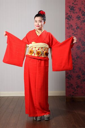 Large sleeves on traditional red Japanese kimono robe garment complete with obi sash being modelled by beautiful young asian oriental model with kanzashi hair flower.の写真素材