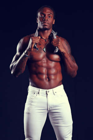 fit black male with super muscular abs, wearing white jeans, against a black backgroundの写真素材