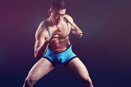 muscular Asian man in a skimpy wrestlers uniform against a black background