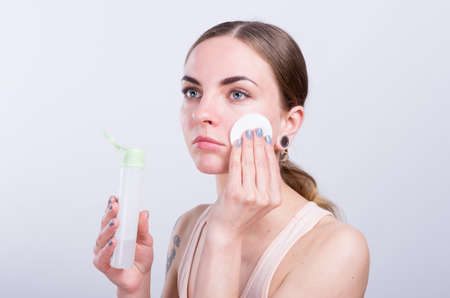 Beautiful young woman cleansing her face with cotton spongeの写真素材