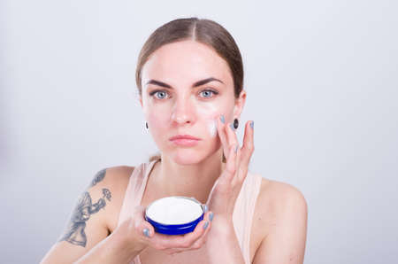 Beautiful young woman puts cream on her face.の写真素材
