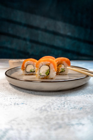 A portion of Japanese Philadelphia sushi roll with avocado and salmon on top. Served on an elegant plate with chopsticks. Side view Photo for advertising bannerの写真素材