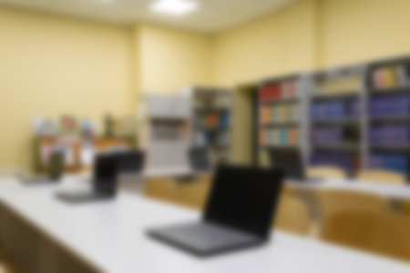 Blurred photo of an empty school library with laptops on tables. Abstract light bokeh on the background of a school interior for designの写真素材