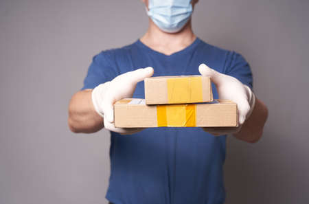 Hand of a white man in a medical rubbe glove r and mask with two parcels on a gray backgroundの写真素材