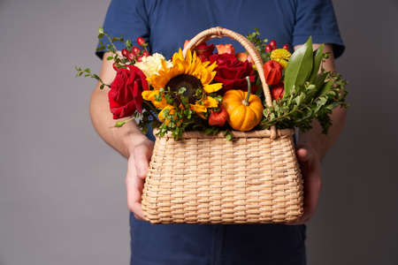 A white man in a blue t-shirt holds out a basket of flowers with a copy space on a grey background, flowers deliveryの写真素材