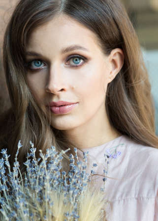 Close up portrait of a beautiful girl with a lavender in a fashionable pink dress stands and smiles on a background with artistic spotsの写真素材