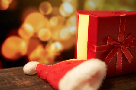 New year's red gift with a bow on a brown wooden table on a gold bokeh background with a copy spaceの写真素材