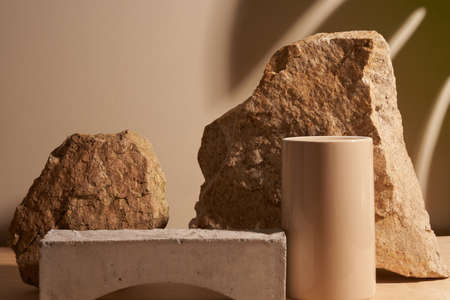 Beige stone and a piece of grey podium tile on a beige background, natural background with shadow of tropical plant for your productの写真素材