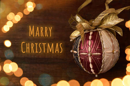 Card with beautiful Golden Christmas hand made ball, luxury decoration on wooden old brown background with bokeh lights and text Merry Christmasの写真素材