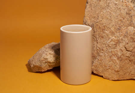 Beige ceramic podium with stones on a yellow background, natural podium, product displayの写真素材