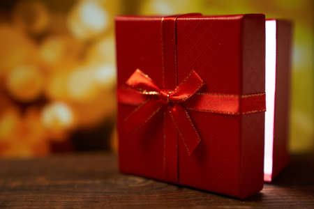 New year's red gift with a bow on a brown wooden table on a gold bokeh background with a copy spaceの写真素材