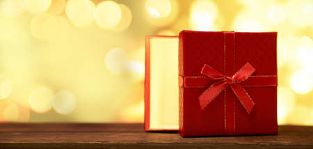 Red gift with a bow and with light inside on a brown wooden table on a gold bokeh background with a...